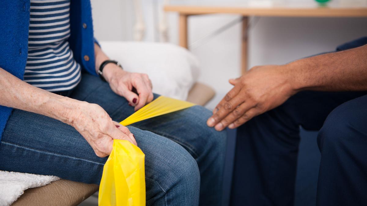 A physio works with a seated patient who is using a resistance band