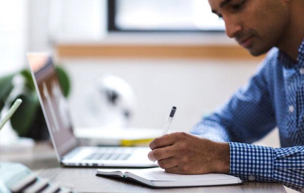 Man taking notes next to a laptop